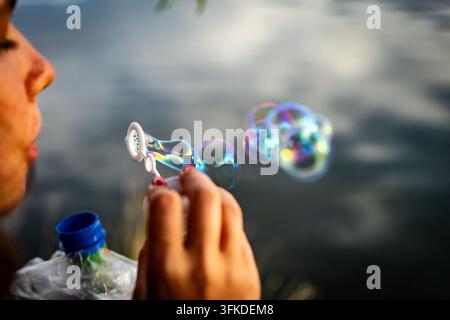 Colorful bubbles trail from the wand in a lively arc. The floating orbs show delicate films and soft reflections while the lake beyond adds calm balan Stock Photo
