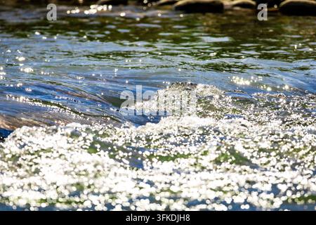 Shifting ripples spread across a shallow stream while floating sparkles cluster near the frame. Soft highlights and flowing lines suggest relaxation p Stock Photo