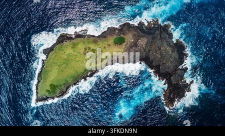 Aerial view of a small green rocky island surrounded by deep blue ocean Stock Photo
