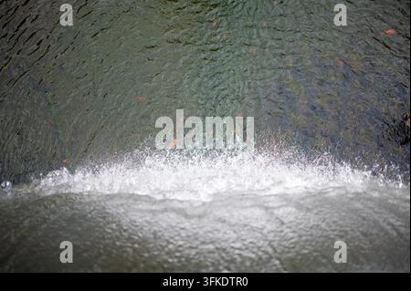 High-angle view from the edge of a waterfall, looking down at rushing white water and foamy spray cascading into a pool below, with ripples and curren Stock Photo