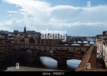 The medieval Ponte Vecchio bridge with its shops spans the Arno river, seen from above with the Vasari Corridor roof and bridges beyond under dramatic Stock Photo