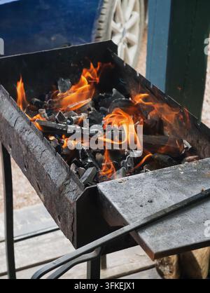 Burning wood and charcoal with a bright orange flame inside a metal grill. The wood logs and coals burn inside the grill, generating heat. Flames engu Stock Photo