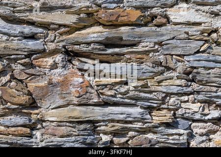 Stacked slate stones forming weathered facade on exterior wall. Stock Photo