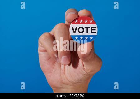 close-up of the word vote framed by white stars on a round badge held between the fingers of a man, its red and blue design evoking the american flag Stock Photo