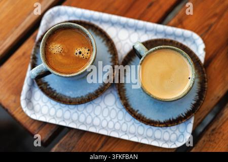 Directly above view of two cups of hot fresh espresso coffee with crema served on a small patterned tray on a rustic wooden table. Stock Photo