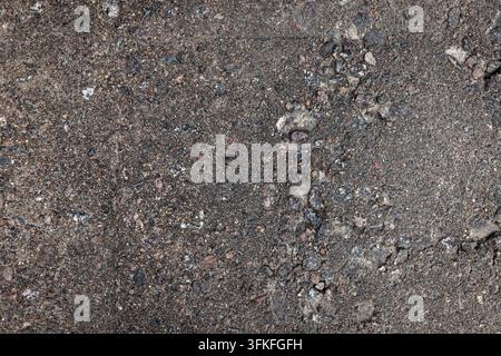 High-resolution close-up of weathered asphalt pavement showing exposed aggregate, grit, small stones and cracks. Ideal for backgrounds, texture overla Stock Photo