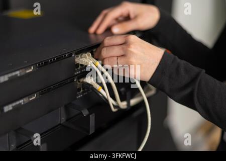Adult IT technician maintains network equipment by connecting and configuring servers in a data center Stock Photo