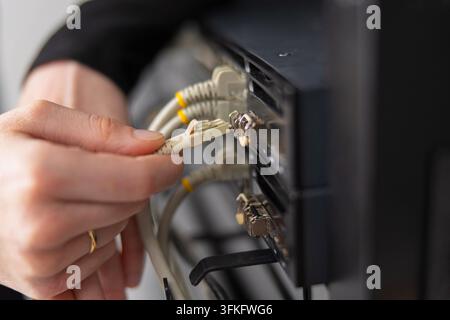 Adult IT technician maintains data center by connecting network cables to a server rack for troubleshooting and updates Stock Photo