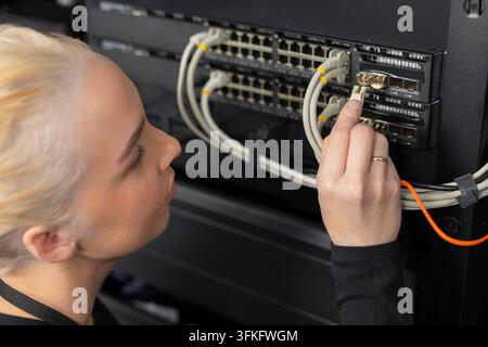 Female IT technician in a data center working with network switches and cables Stock Photo