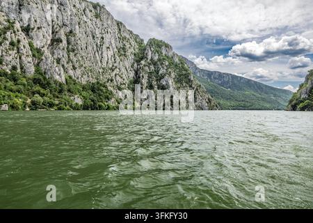 Danube river flows through the majestic Iron Gates gorge, framed by towering rocky cliffs & lush greenery Serbia & Romania Stock Photo