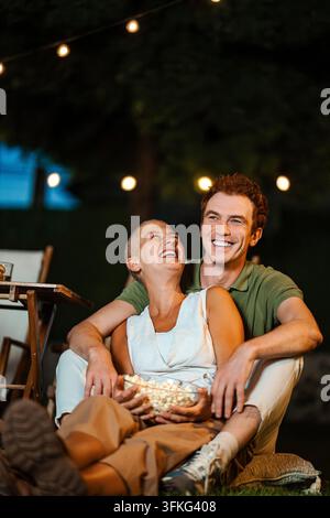 Happy couple enjoying outdoor movie night with popcorn Stock Photo