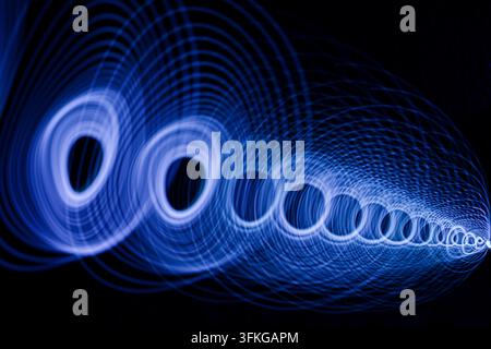 Glowing blue circular light pattern moving across a dark space. Stock Photo