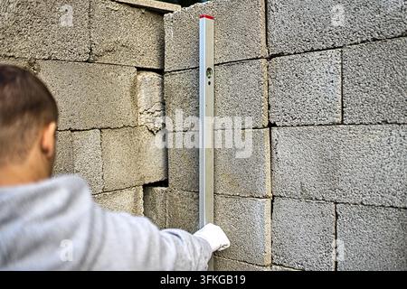 Close-up of a mason using a spirit level to check the vertical alignment of a newly built concrete block wall during construction work. Stock Photo