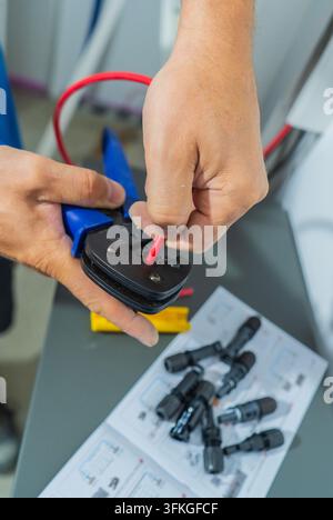 Electrician using wire stripper to prepare red electrical cable for connector assembly during electrical installation work in Germany. Stock Photo