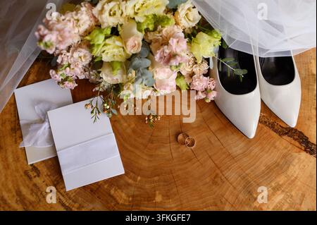 Elegant bride accessories flat lay on wooden slab background, white shoes, wedding rings, invitations, bouquet showcasing romance, quiet luxury, minim Stock Photo