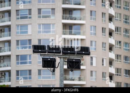 A cluster of powerful black LED floodlights mounted on a metal pole stands in front of a modern multi-story residential apartment building. Stock Photo