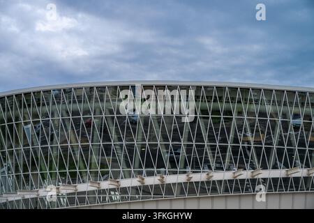 A curved modern building facade featuring a striking geometric lattice of white triangular framing and reflective glass panels beneath an overcast, cl Stock Photo