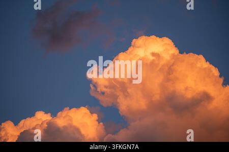 Glowing orange sunset clouds against deep blue sky, dramatic cloudscape with copy space, warm evening light and atmospheric texture background. Stock Photo