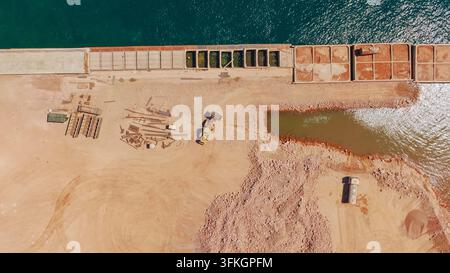 Bulldozer and building materials on a large industrial port development site next to the ocean, showing ongoing progress for future maritime activitie Stock Photo
