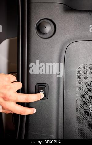 Pressing trunk release switch carefully. Closeup of hand activating vehicle trunk latch. Everyday scene showing driver securing cargo by pressing Stock Photo