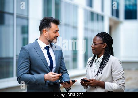Diverse business professionals discussing work using tablet outdoors Stock Photo