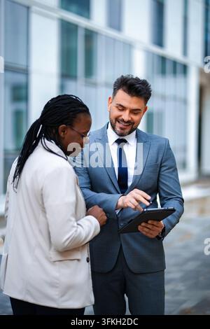 Diverse business professionals collaborating using digital tablet outdoors Stock Photo