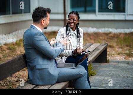 Business colleagues collaborating outdoors on digital devices Stock Photo