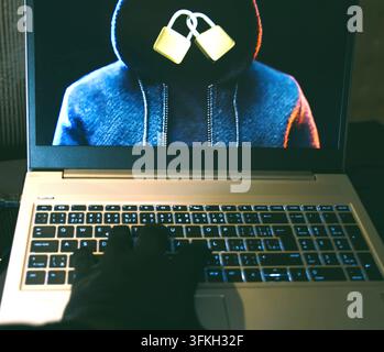Conceptual cybersecurity concept showing a hacker typing on a laptop with digital lock graphics on screen. Stock Photo