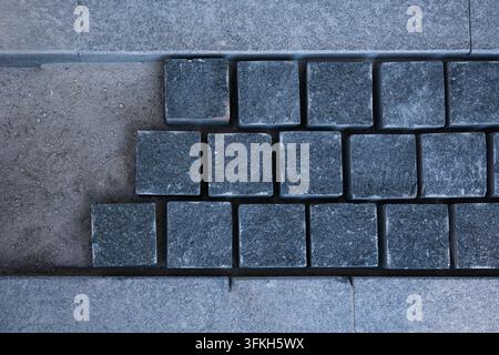 High angle top view of dark grey granite cobblestone paver blocks being installed on sand bedding with copy space during outdoor sidewalk construction Stock Photo