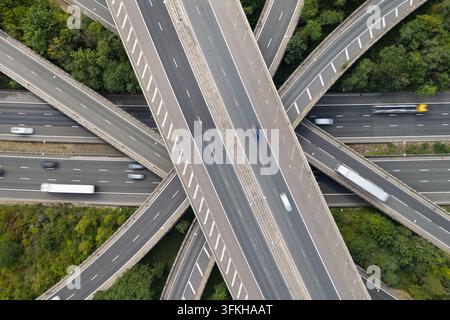 Aerial view of constant traffic flowing across a multi-level highway interchange surrounded by lush green forests. Stock Photo
