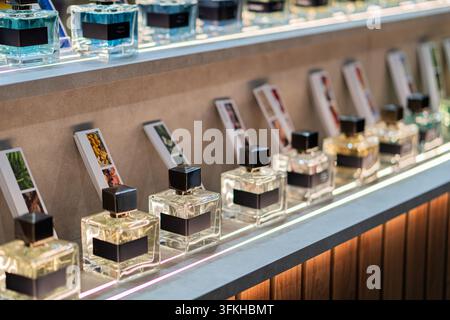 Perfume bottles collection on sleek dark gray shelf, clear glass with black caps and labels, dynamic arrangement, minimalistic light background, soft Stock Photo