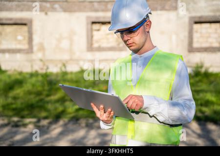 Architect in safety vest and hard hat using tablet at renovation site. Digital construction management paperless planning and project documents. Stock Photo