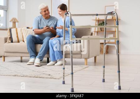 Elderly care and home assistance, senior man with caregiver using smartphone and mobility walker for independent living and health support in living r Stock Photo