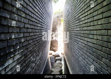 Narrow light and shadow path between high gray brick walls Stock Photo