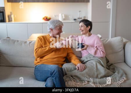 Happy senior married couple drinks tea and laughs together sitting on comfortable home sofa Stock Photo