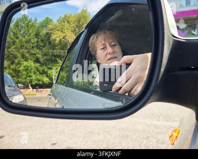 Woman sits in a car and takes a selfie while looking at the camera. She is alone and relaxed in the moment. Stock Photo