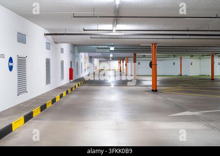 Wide angle view of empty underground parking garage interior featuring bright overhead lights orange support pillars painted yellow curb and concrete Stock Photo