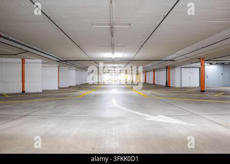 Wide angle perspective view of empty underground parking garage interior showing painted white curved arrow on concrete floor yellow lines orange pill Stock Photo