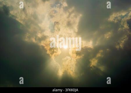 Dramatic bright sun shine breaking through dark cloudy sky with crepuscular sun rays Stock Photo