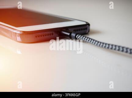 Smartphone connected to a usb charging cable and fast charging on beige background. Phone fast and quick speed charge. Stock Photo