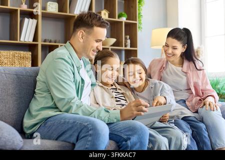 Happy parents with daughters using tablet together on sofa at cozy home interior Stock Photo