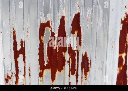 Close-up of a weathered corrugated metal sheet featuring vibrant orange rust stains and peeling paint, creating a gritty industrial texture with a com Stock Photo