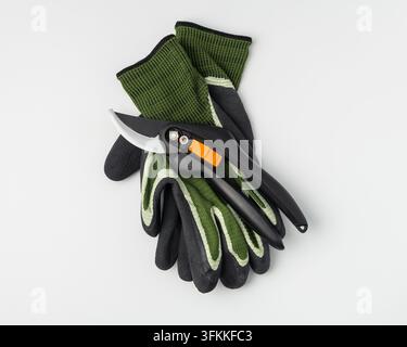Minimalist studio shot of black bypass pruner shears lying on a pair of green protective gardening gloves. High quality horticulture cutting equipment Stock Photo