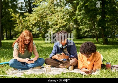 Multiethnic Teenagers Using Smartphones While Sitting in Park Stock Photo