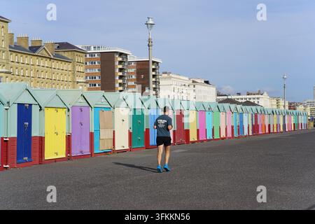 Runner jogging past a long row of colourful beach huts on the Hove seafront, Brighton, England. Stock Photo