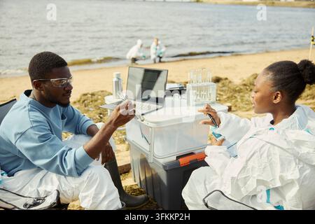 Black Ecologists Analyzing Water Samples on Shoreline Stock Photo