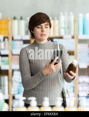 Woman in autumn clothes scans code on cough syrup to check the expiration date Stock Photo