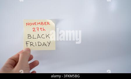 Hand placing a yellow sticky note with black friday and november 27th written on it Stock Photo