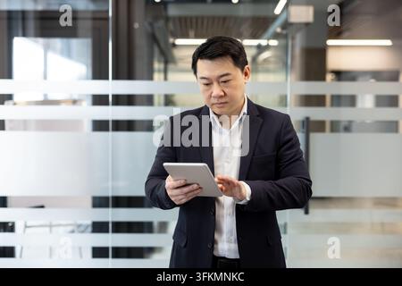 Businessman using a tablet in a modern office for financial analysis and business management. Professional man checking digital documents on a mobile device to improve corporate communication. Stock Photo