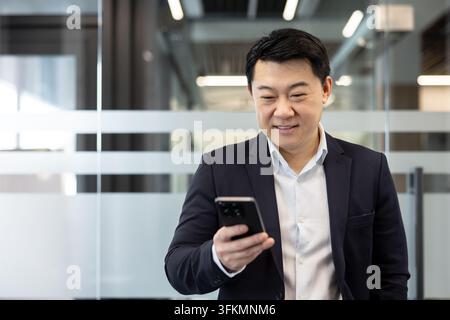 Businessman using smartphone for mobile communication in a modern office. Professional man checking messages on his phone to manage corporate connectivity and digital business technology tasks. Stock Photo